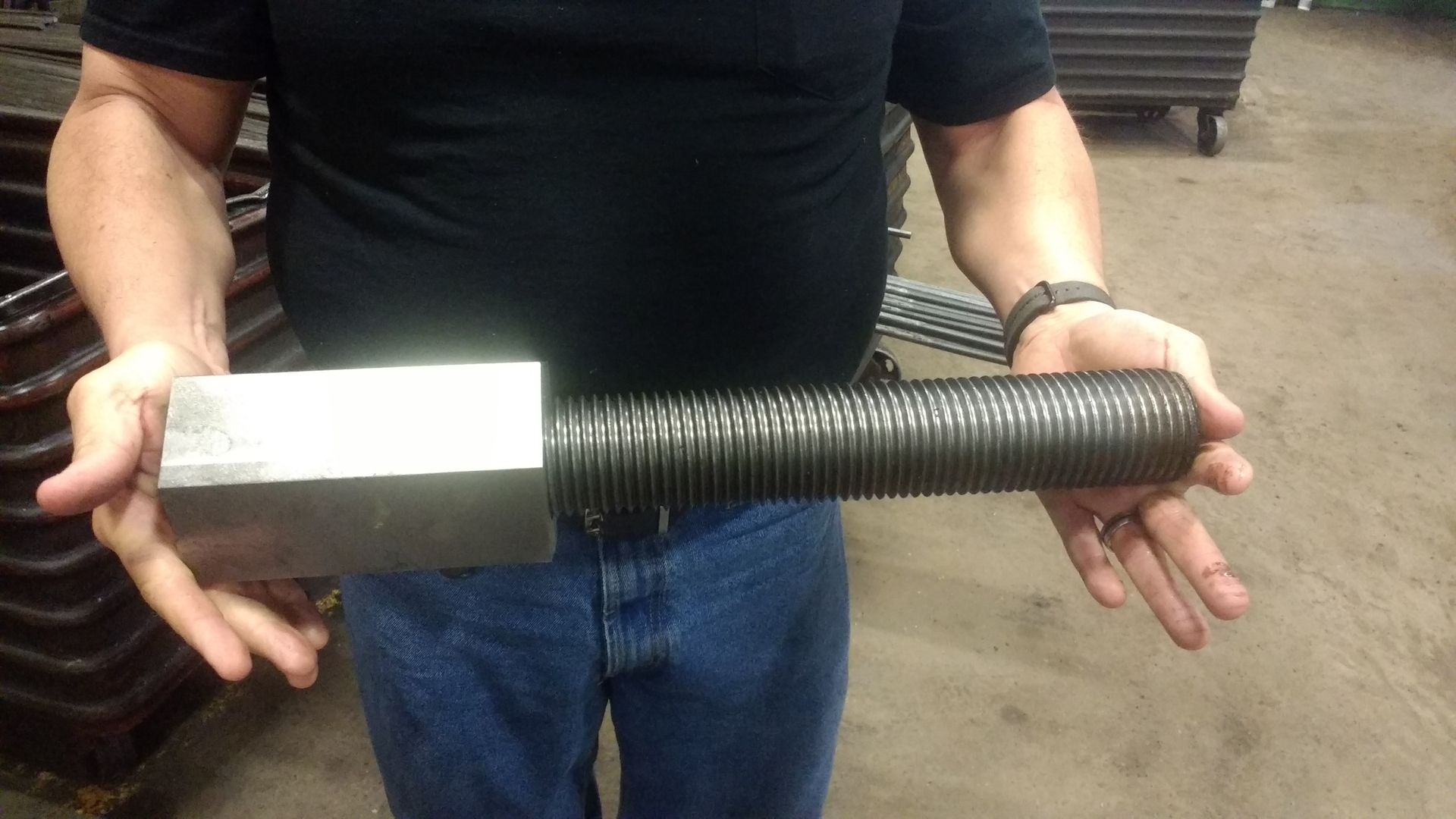 Man holding a large, industrial bolt with a square head and threaded shaft.