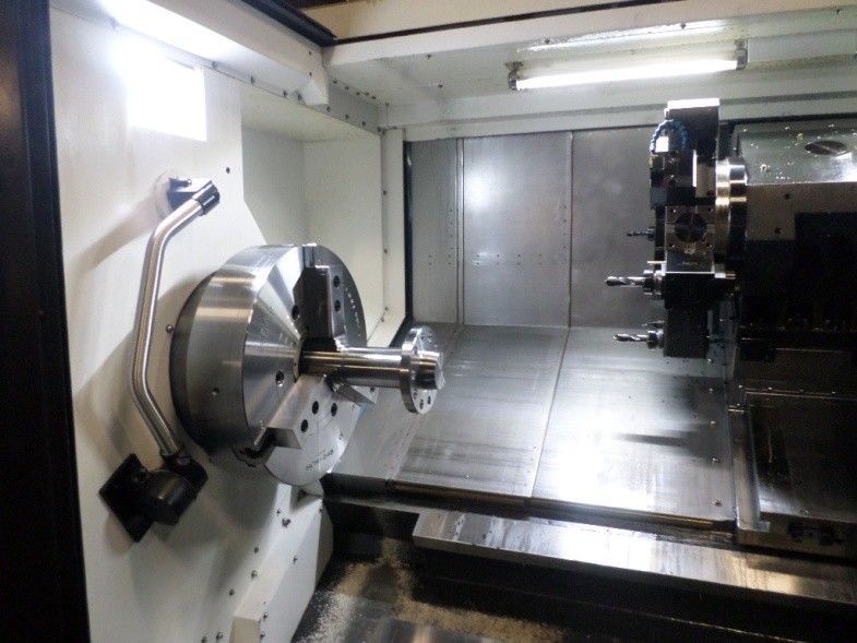 Inside of a CNC lathe, with a metal rod clamped in the chuck, ready for machining.