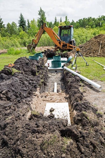 An excavator installing a septic system in a grassy field; dirt piles around the trench.