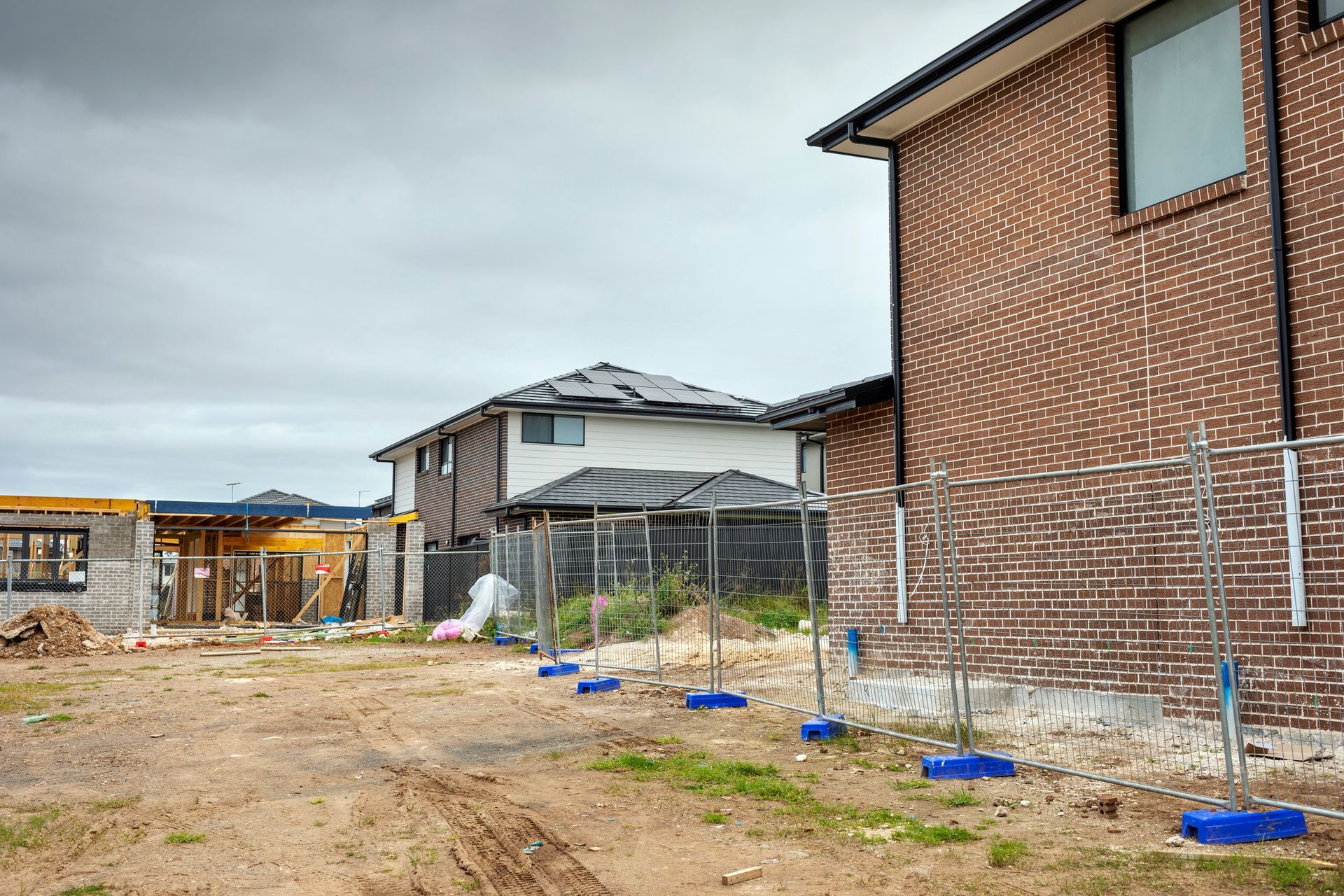 Houses under construction, brick and unfinished siding, overcast sky, dirt lot.