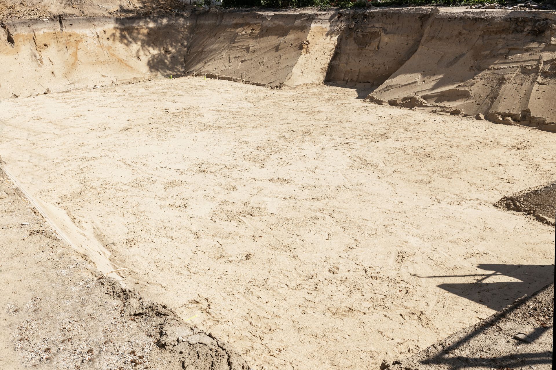 An excavated, rectangular pit with light-colored, sandy soil. Uneven walls and a shadow at the bottom right.