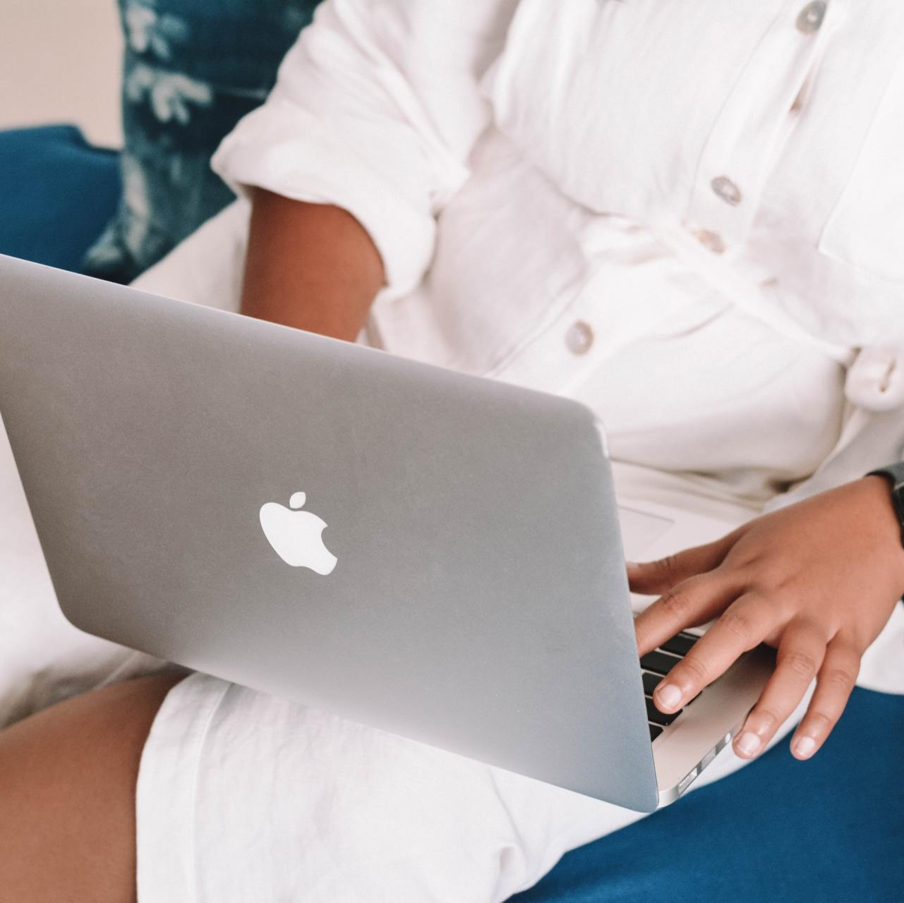 Person in white outfit using a laptop with an Apple logo on their lap.