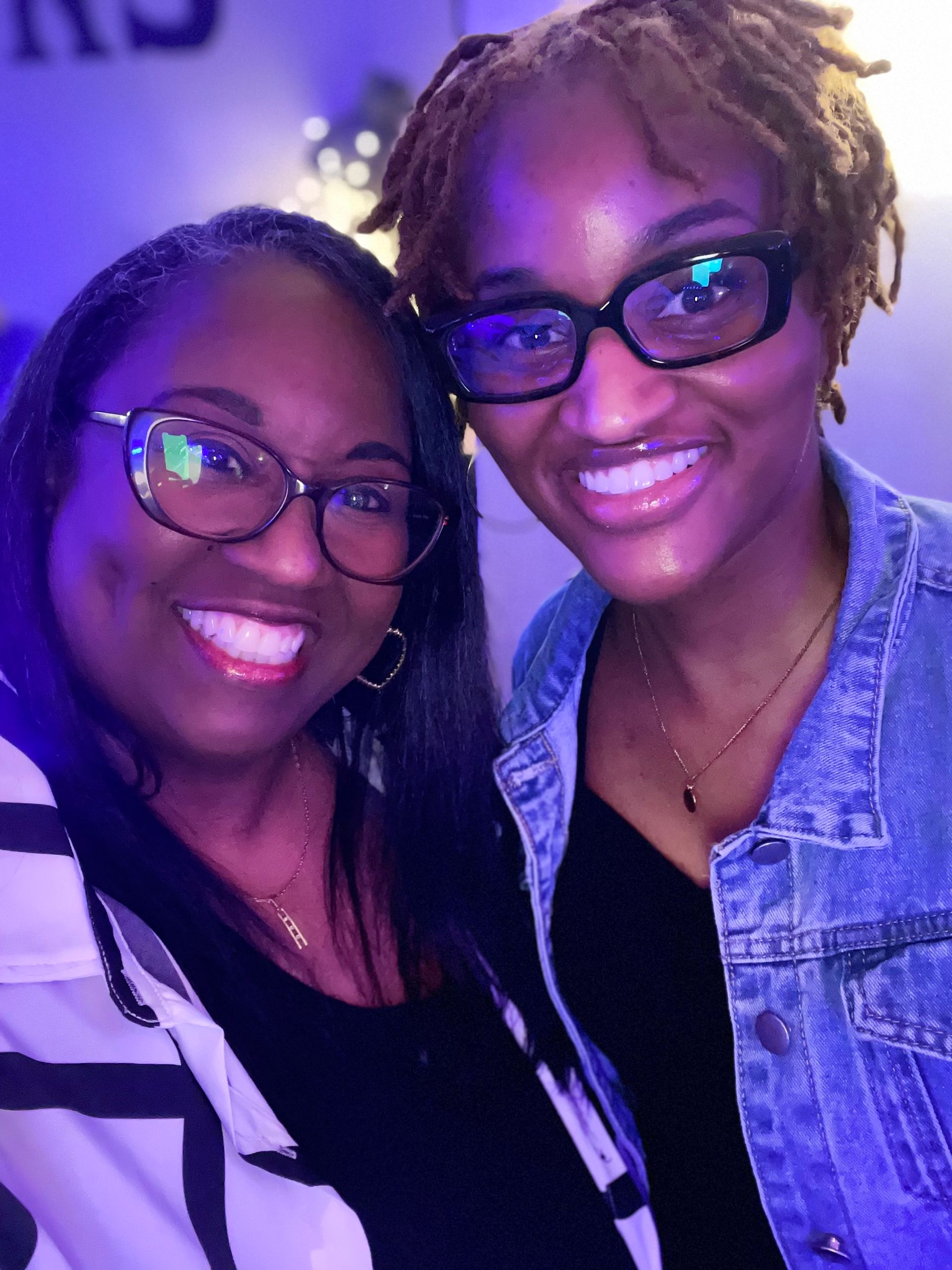 Two women wearing glasses and a denim jacket are posing for a picture.