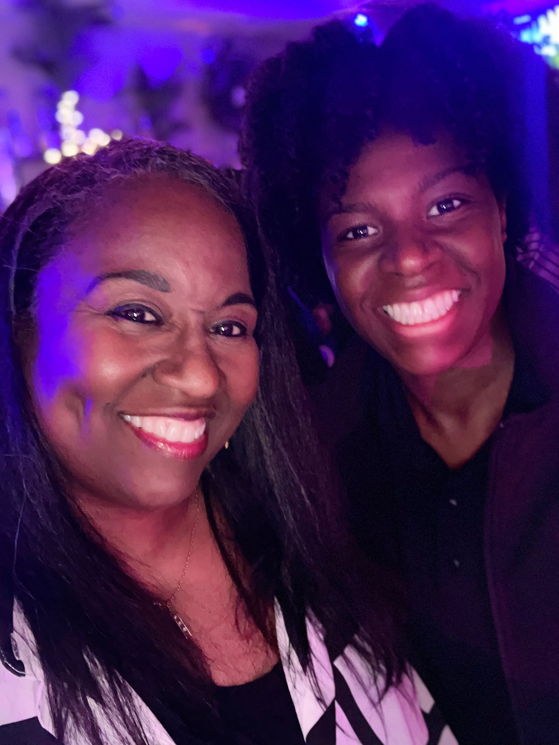 Two women are smiling for a picture in front of purple lights.