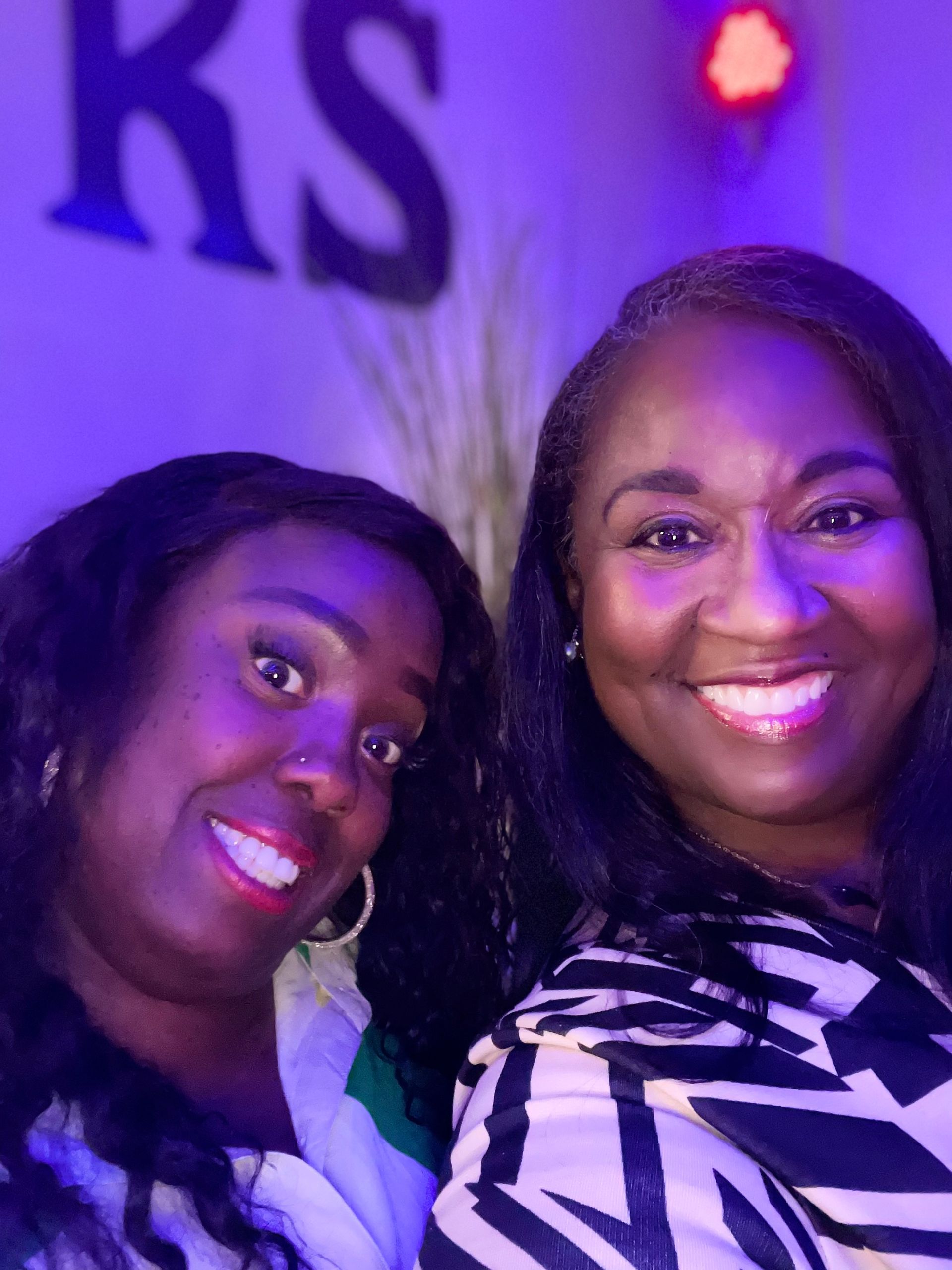 Two women are posing for a picture in front of a sign that says ks.