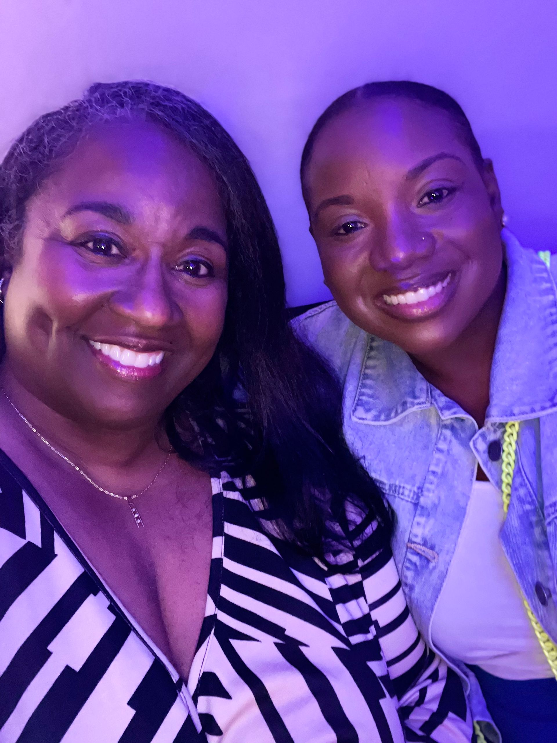 Two women are posing for a picture in front of a purple wall.