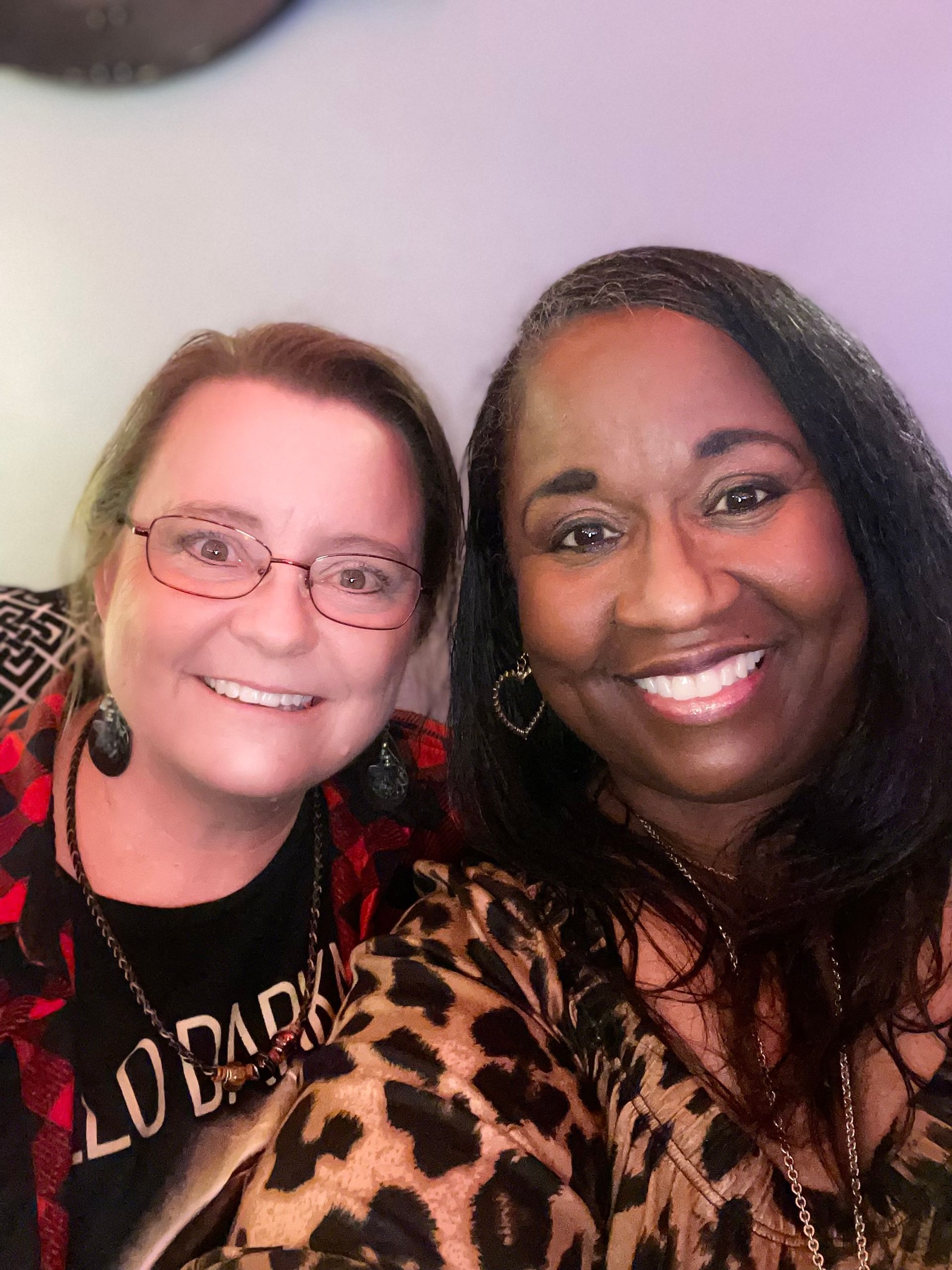 Two women are posing for a picture and one of them is wearing a leopard print shirt.