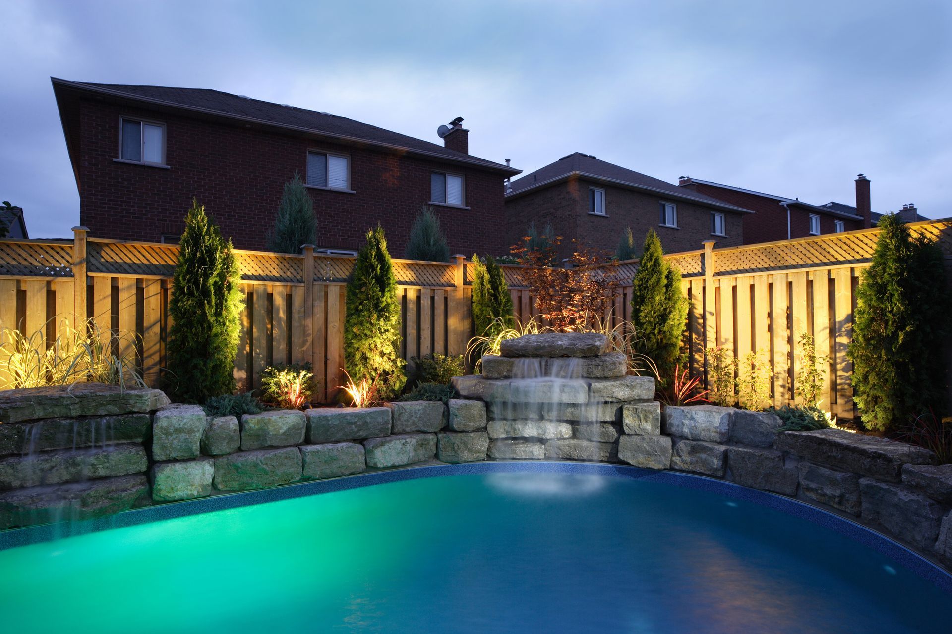 A swimming pool with a waterfall in the backyard of a house.