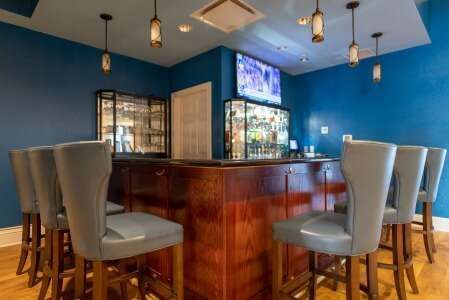 A bar with wooden counter, blue walls, and gray bar stools. Television and liquor cabinets are visible.