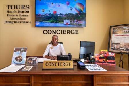 A concierge sits at a desk in front of a screen displaying hot air balloons.
