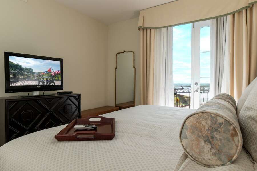 Bedroom with a large bed, TV, and a door opening to a balcony with city view.