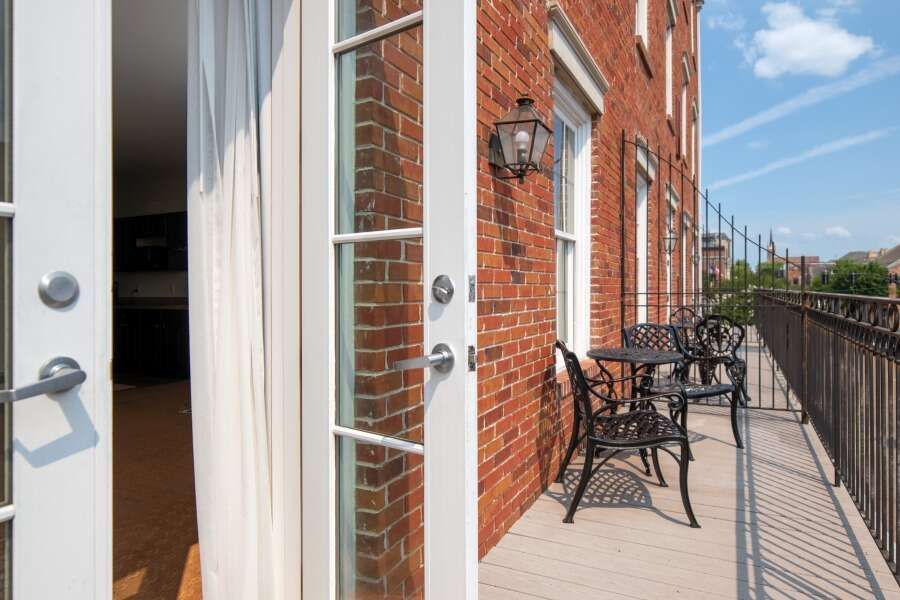 French doors open to a brick balcony with black furniture; sunny day with blue sky.