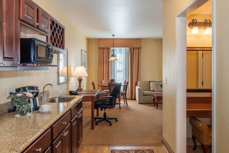 Kitchen and dining area in hotel suite with brown cabinets, appliances, and furniture.