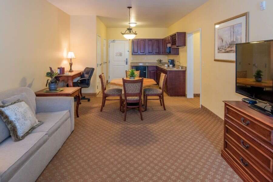 A furnished hotel suite with a sitting area, dining table, kitchenette, and a desk.