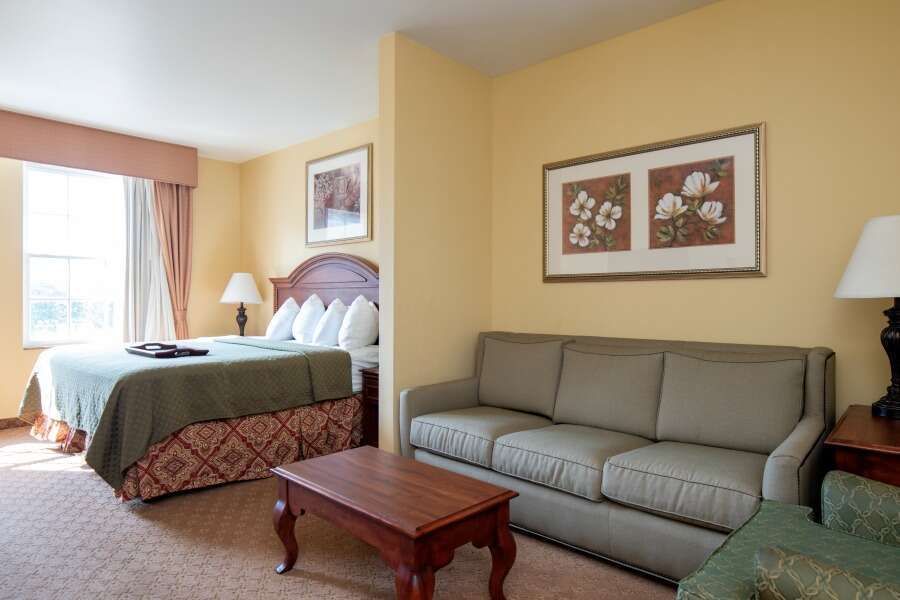 Hotel room with a bed, couch, and coffee table. Yellow walls and neutral colors.