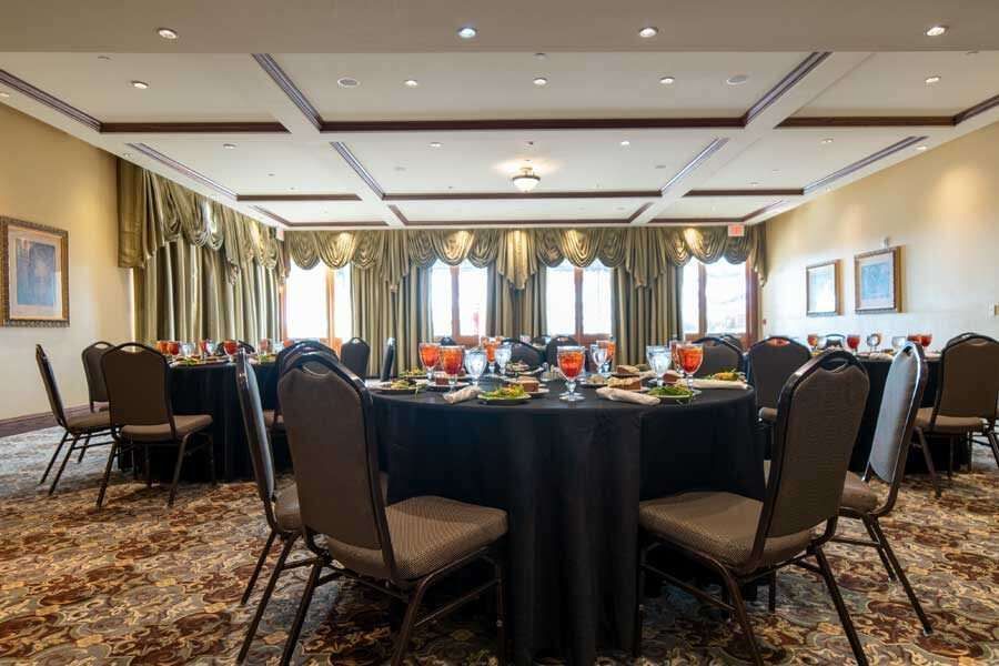 Banquet hall with round tables set for guests, dark table cloths, gold curtains, tan chairs.