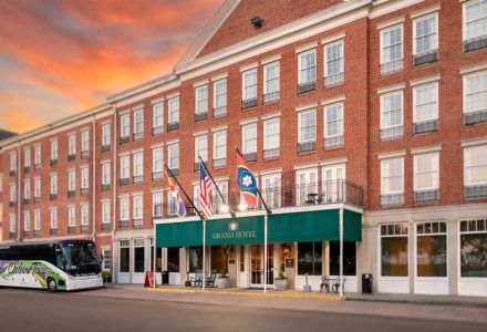 Exterior of the historic L&N Train Hotel with flags, green awning, and a tour bus parked in front.