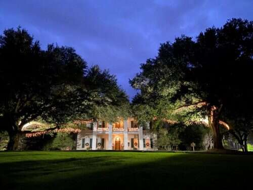 White mansion at dusk with string lights in the trees.