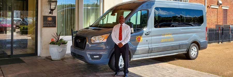 A man in a red tie stands next to a gray van in front of a building.