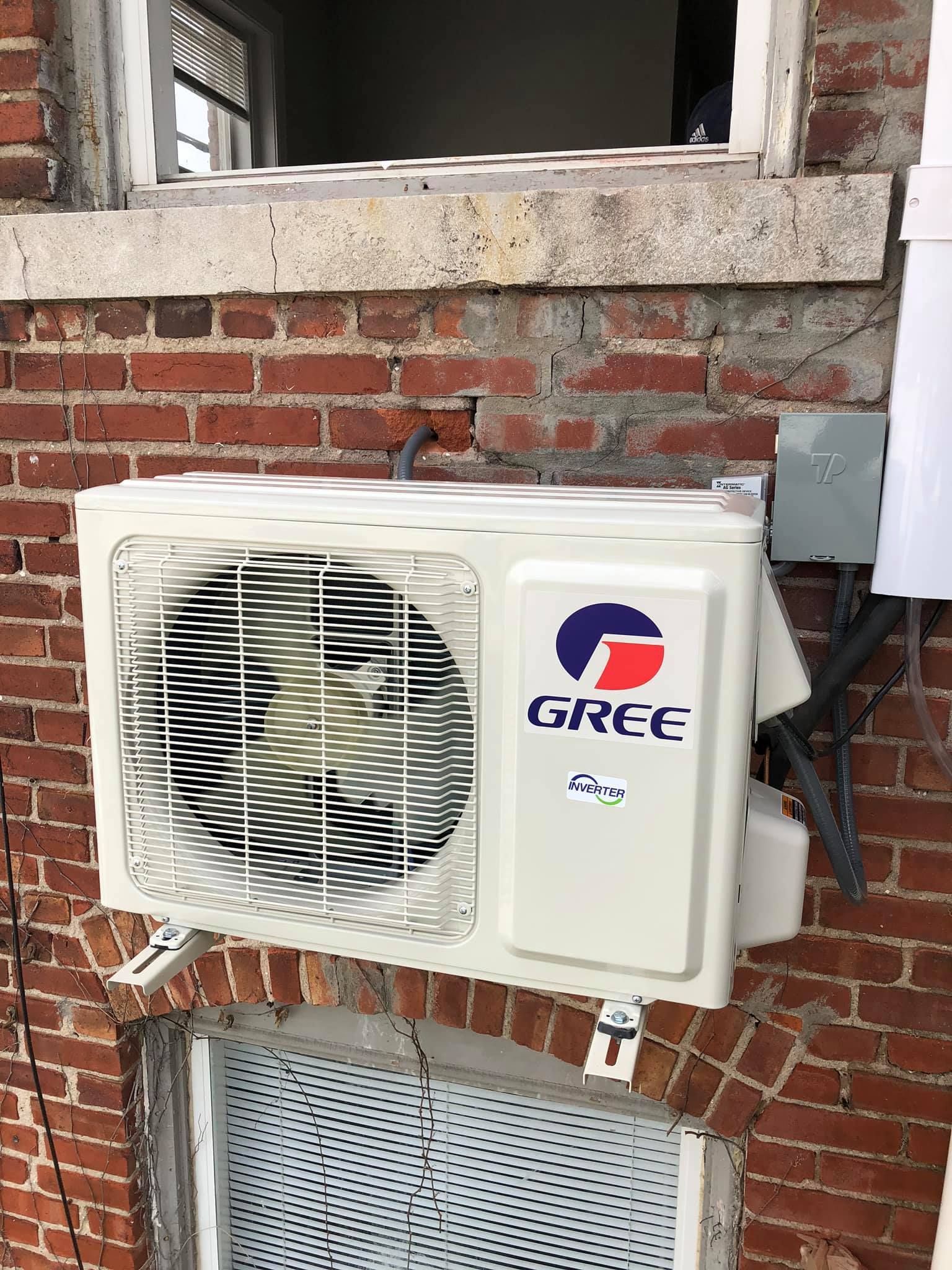 A gree air conditioner is mounted on a brick wall next to a window.