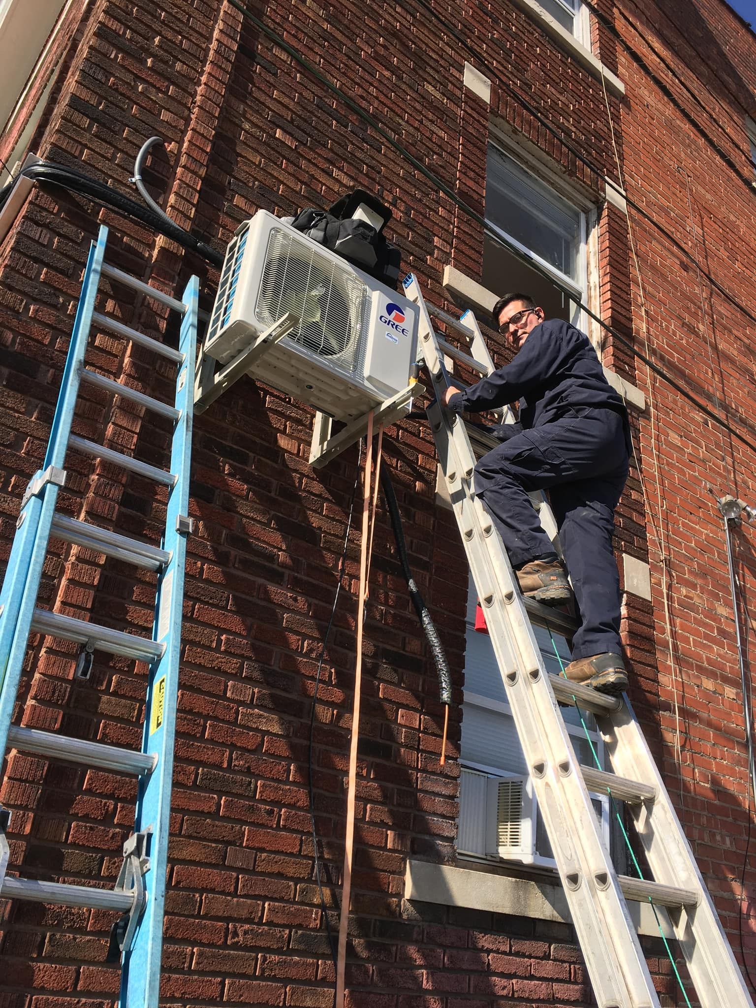 HVAC technician on ladder installing Gree mini split AC on exterior brick wall