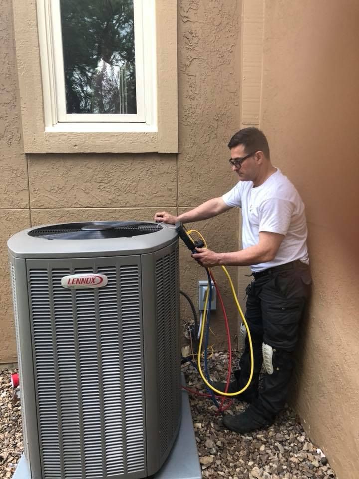 Technician servicing Lennox AC unit with refrigerant hoses connected