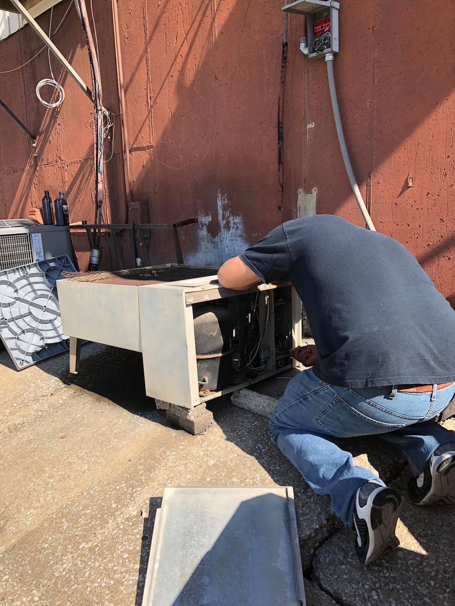 Technician performing HVAC repair on rooftop unit outside commercial building