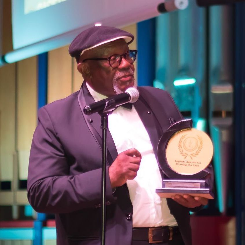 Man in suit, holding award, speaking into microphone on stage.