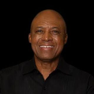 Smiling Black man in a black shirt against a black background.