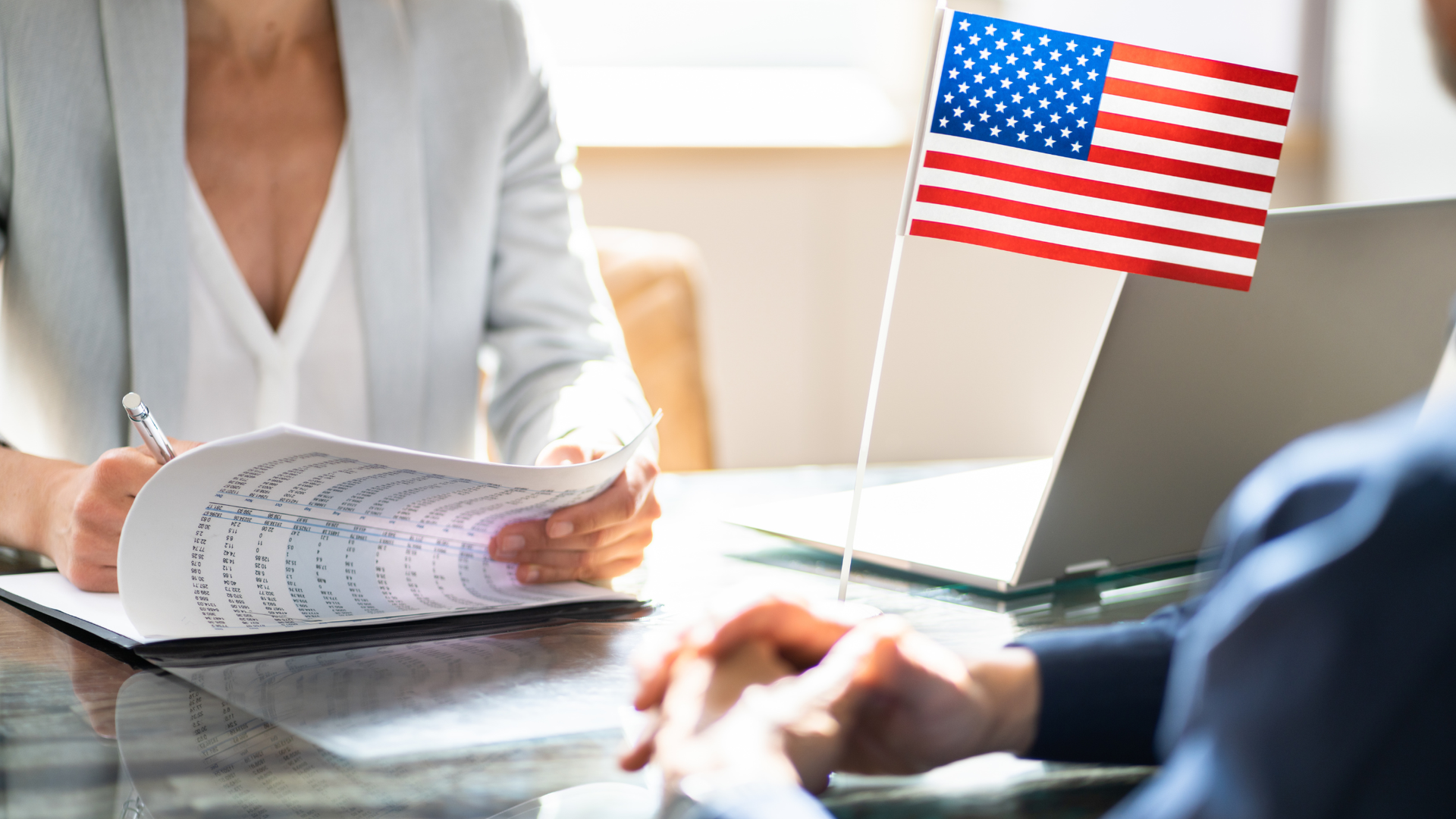 Person signing a document, with a laptop and American flag on the table.