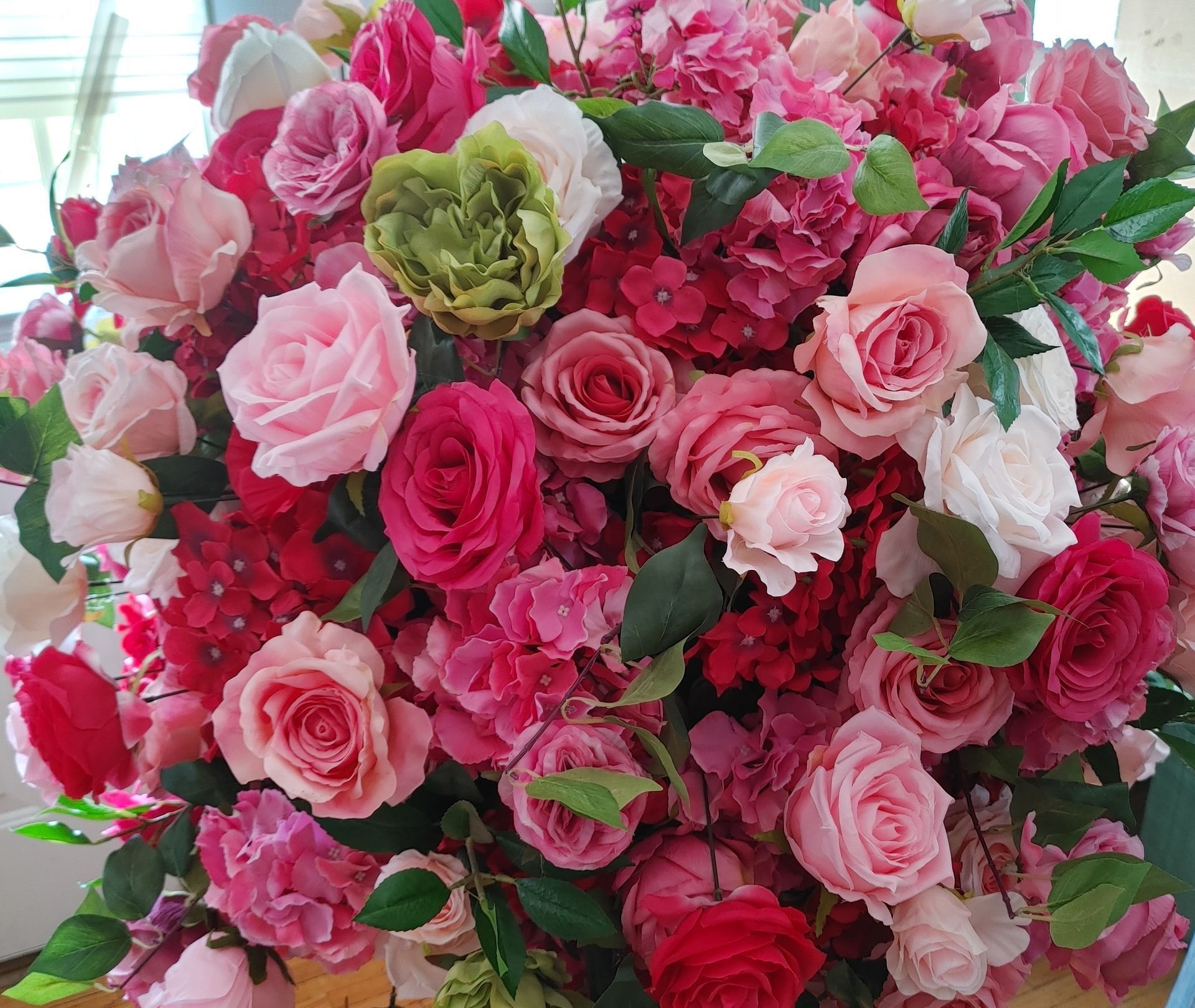 A vase filled with pink and red roses is sitting on a wooden floor.