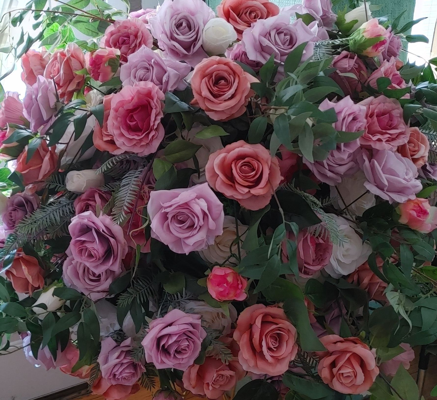 A vase filled with pink and purple roses is sitting on a wooden floor.