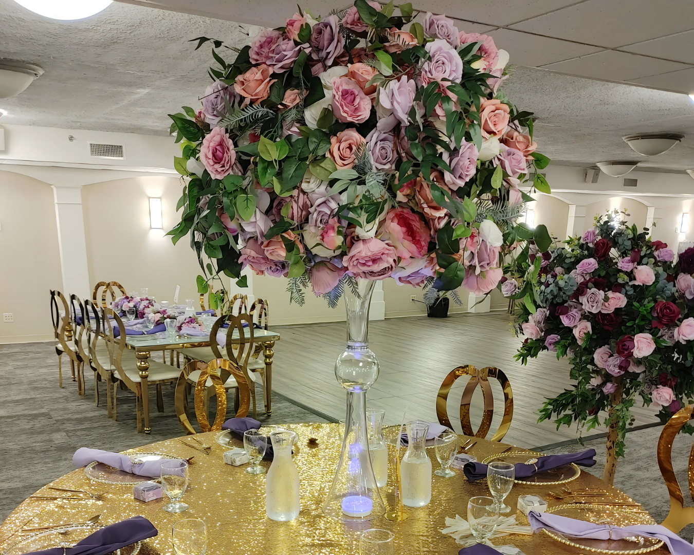 A table set for a wedding reception with a large vase of flowers on it.