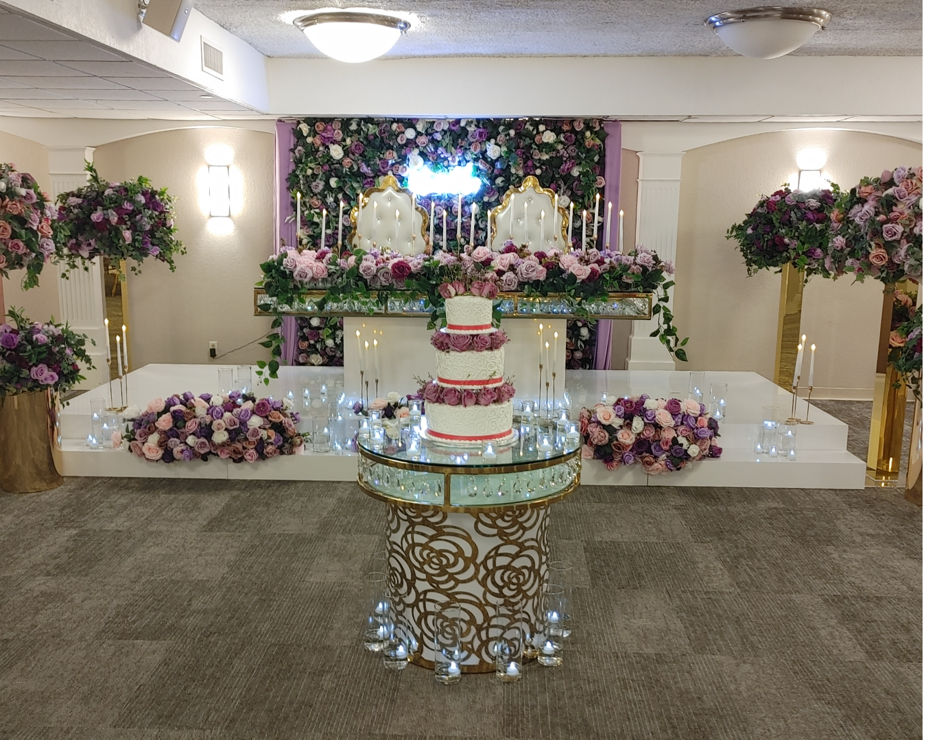 A wedding cake is sitting on top of a glass table surrounded by flowers and candles.