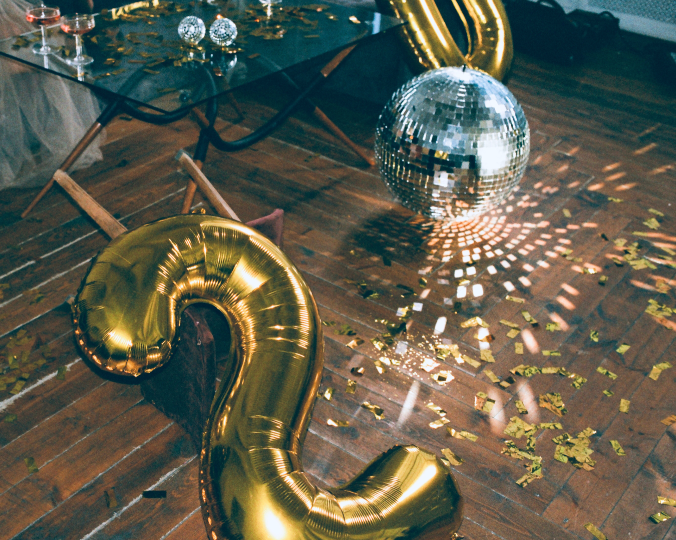 Two gold balloons in the shape of the number 2 are on the floor next to a disco ball.