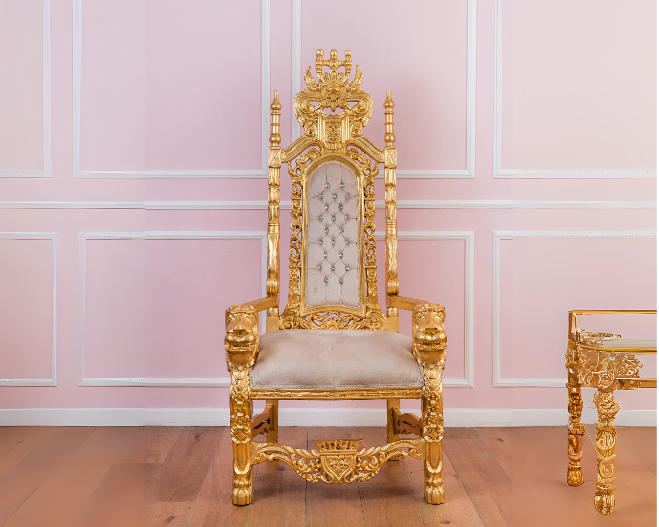 A gold chair is sitting in front of a pink wall.