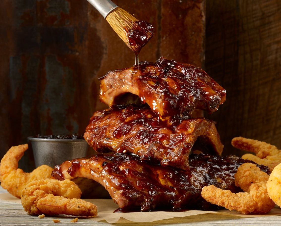 beautiful shot of ribs stacked with bbq sauce being put on top, shot by food photographer rusty hill
