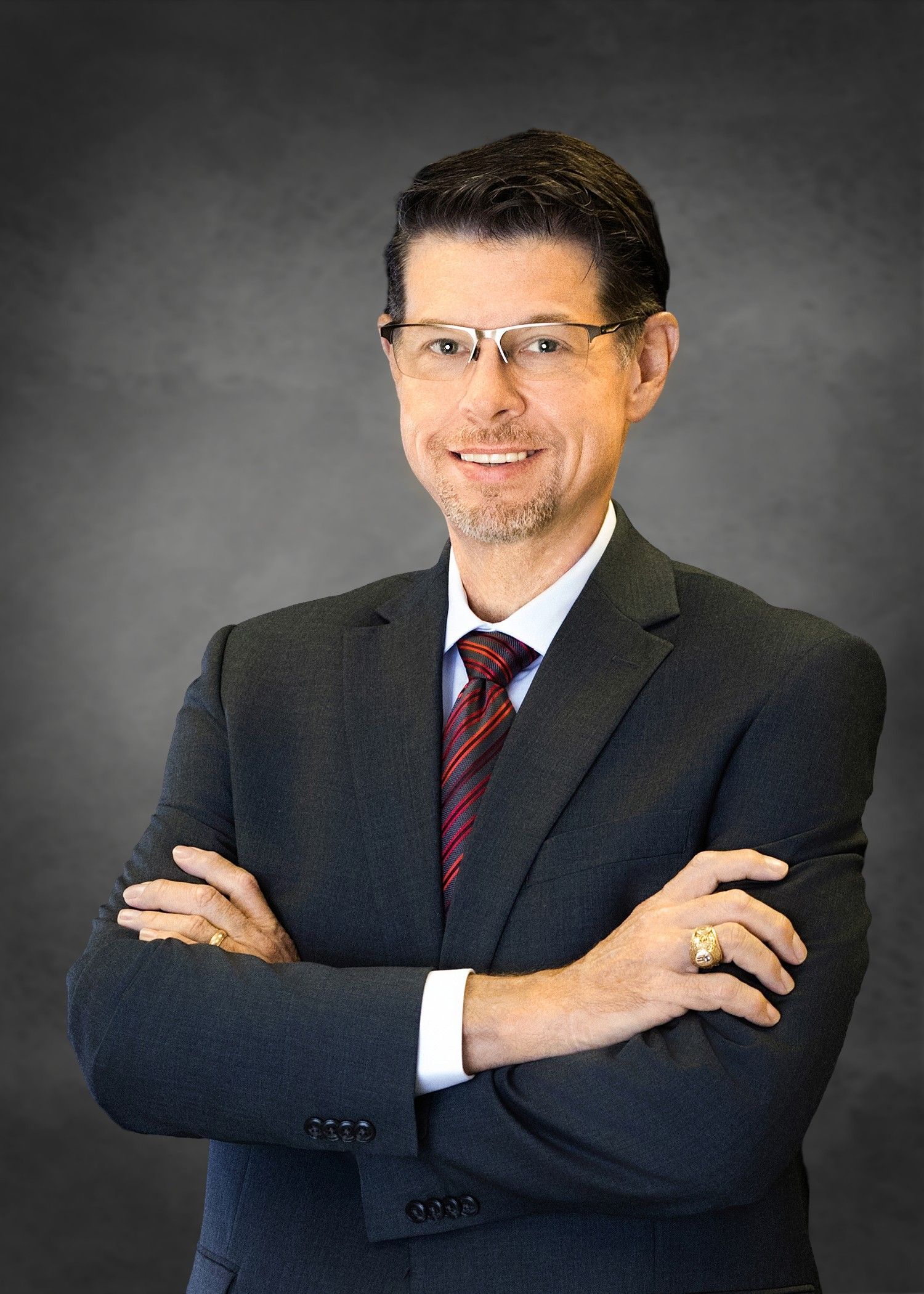 A smiling man with glasses in a dark suit and white shirt, looking towards the camera.