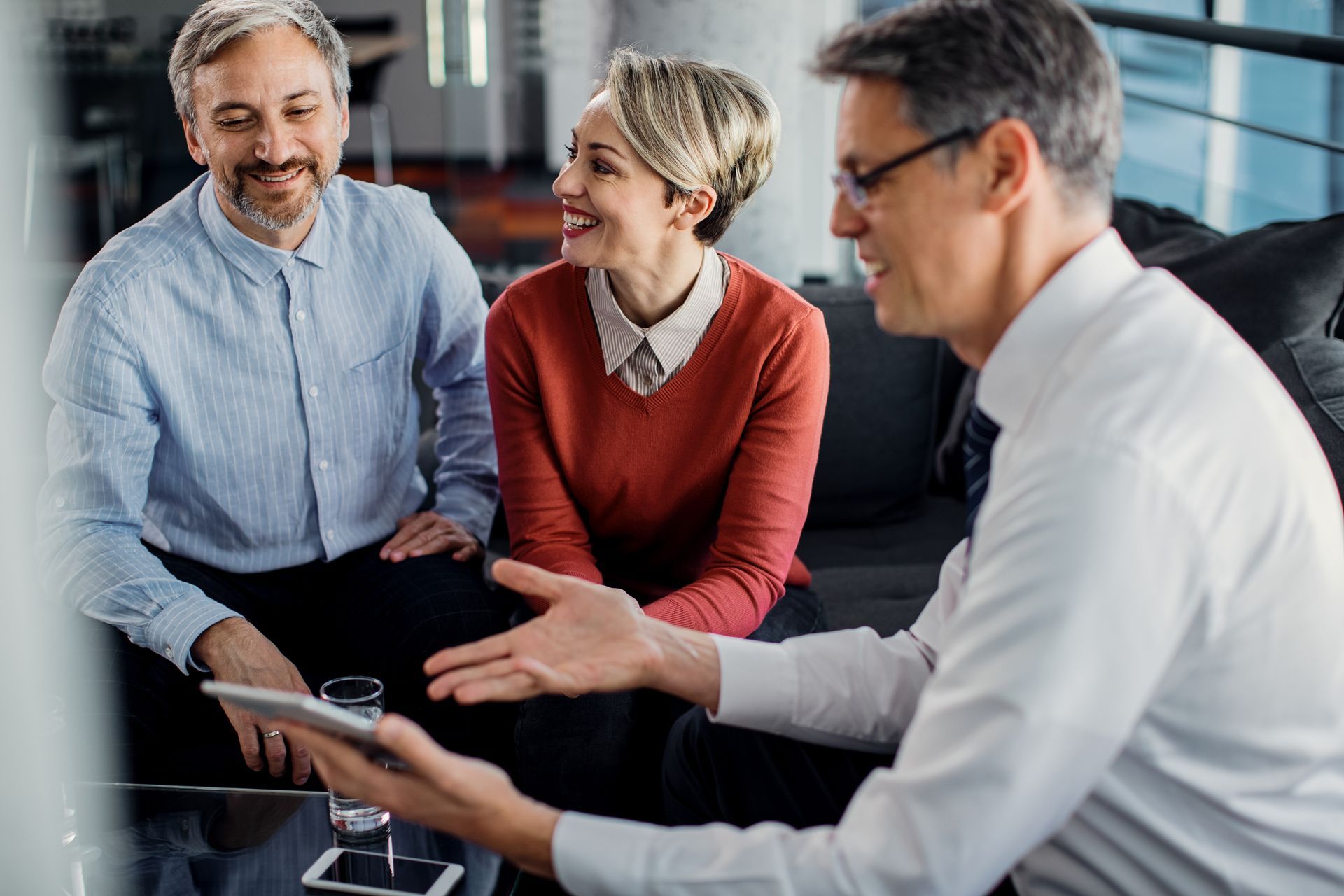A financial advisor shows a tablet to a smiling couple in an office setting.