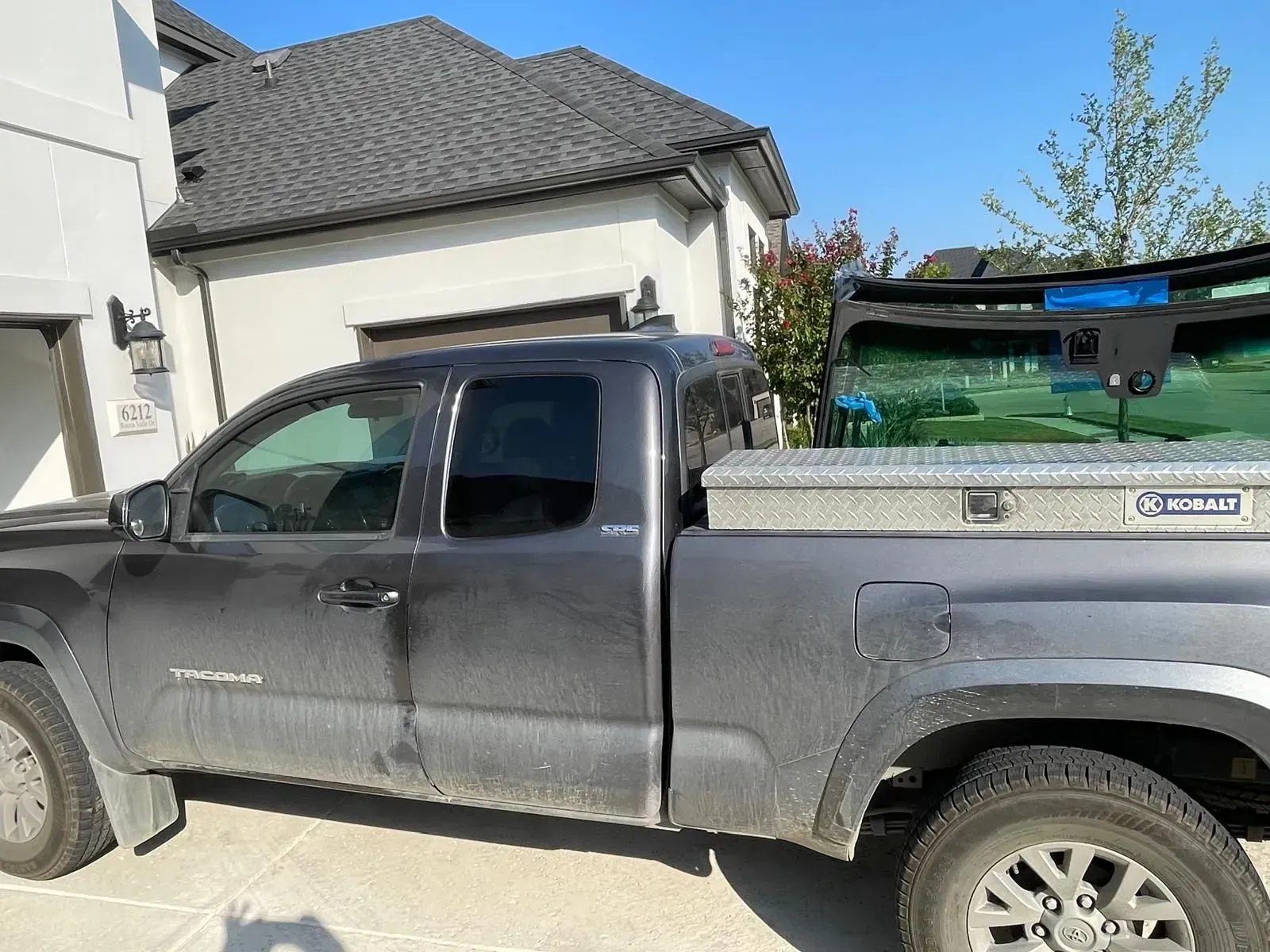 Gray pickup truck parked in front of a light-colored house with a toolbox in the bed.