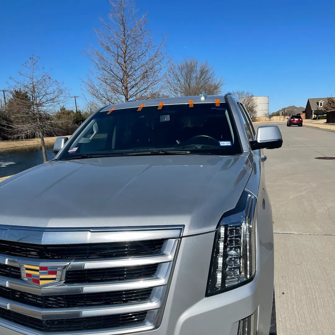 Silver Cadillac SUV parked on a street, with a clear blue sky and a few trees in the background.