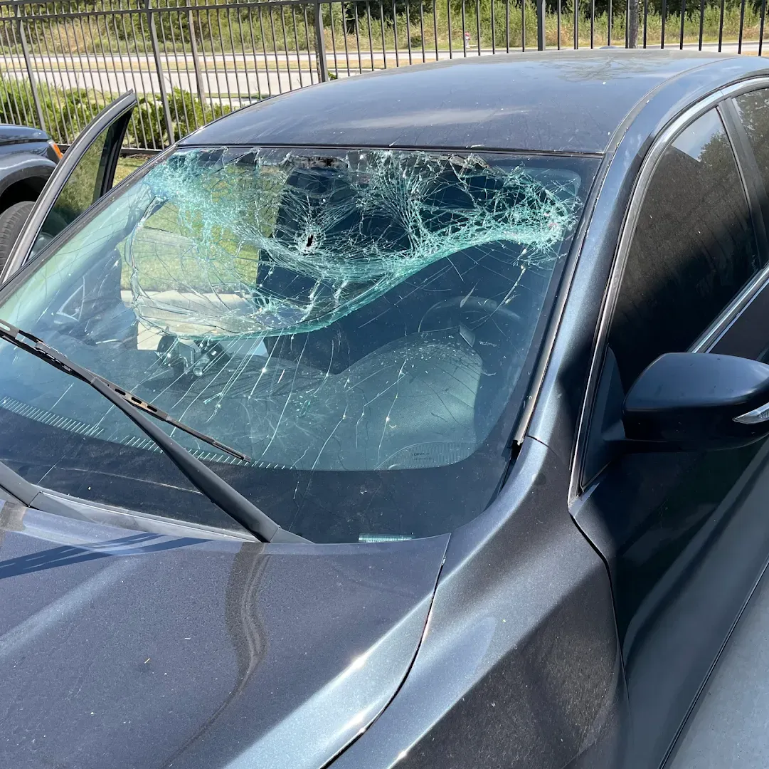 A dark gray car with a severely damaged windshield, its glass cracked and shattered.