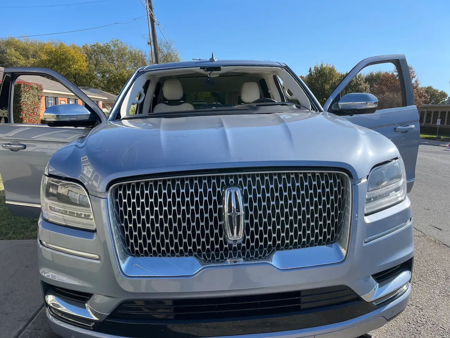 Silver Lincoln Navigator SUV with doors open on a sunny street.