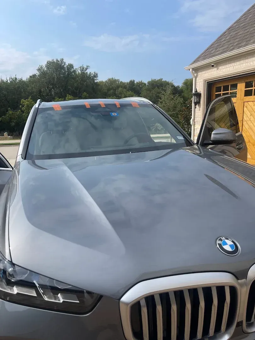 Gray BMW SUV parked in front of a house on a sunny day.