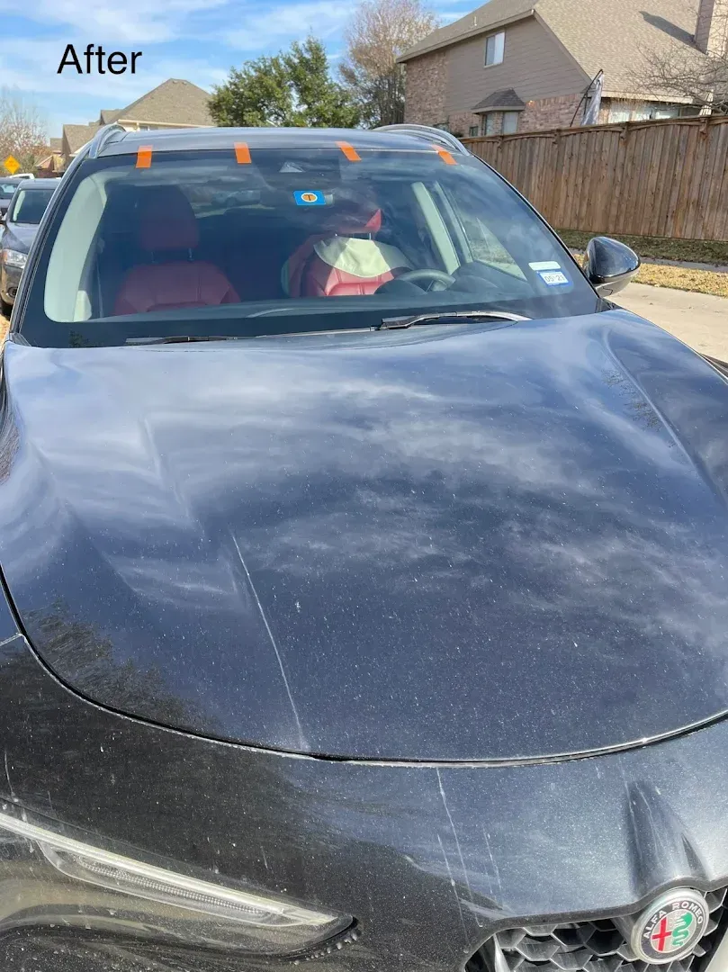 Black car after repair with stickers on windshield, parked on street.