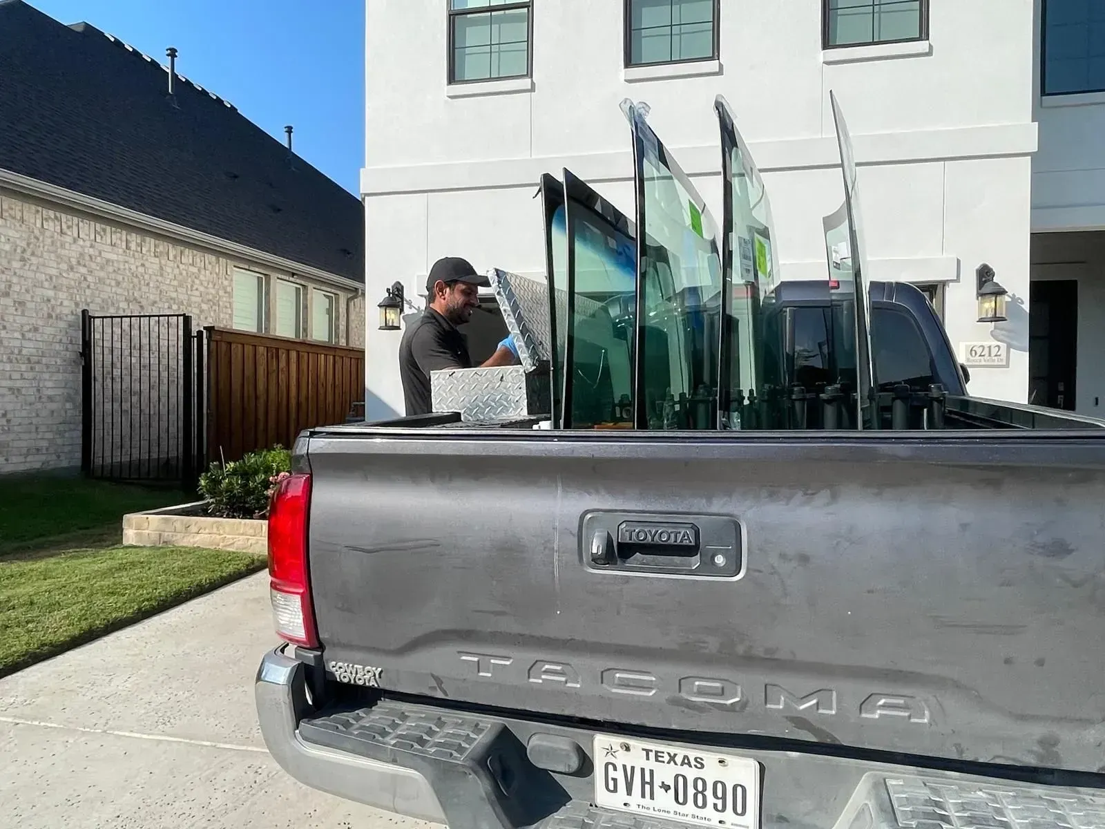 Man loading large glass panels into a gray pickup truck parked in front of a house.