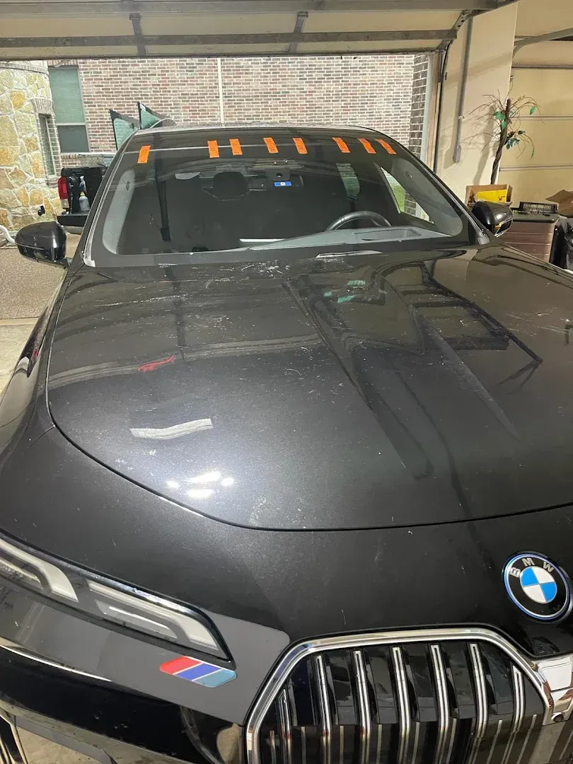 Black BMW with orange tape on windshield, inside a garage.