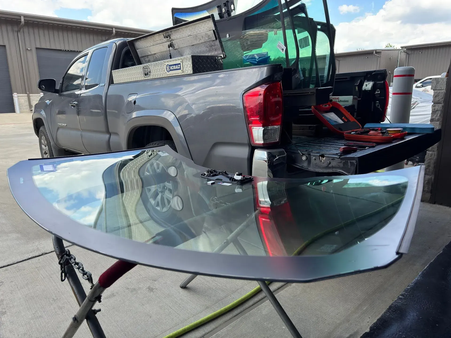 A gray truck with a windshield replacement in progress; new glass on a stand, tools and glass in the bed.