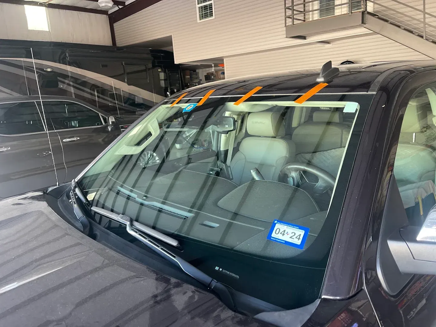 A dark car's windshield with orange tape, likely for repair or replacement, in an auto shop.