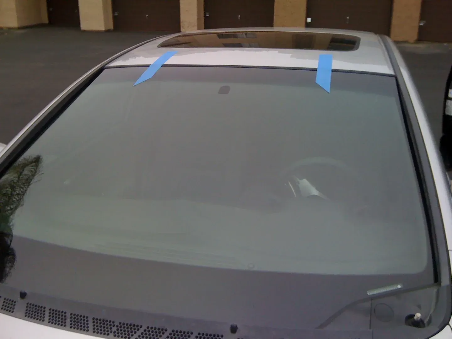 Windshield of a white car with blue tape, partially obscuring view of interior.